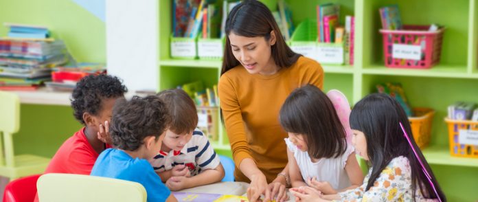 Asian female teacher teaching mixed race kids reading book in classroom,Kindergarten pre school concept.